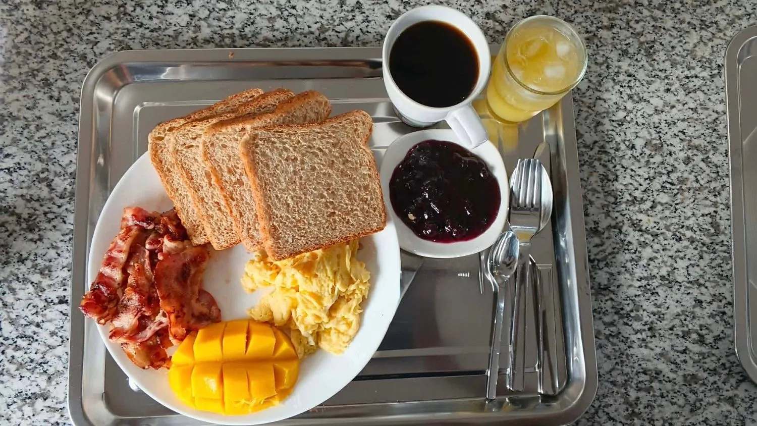 American set at OIA Suites Moalboal: bacon, scrambled eggs, whole-wheat toast with jam, fresh mango, coffee and orange juice